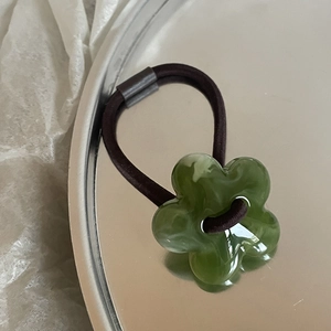 Macro shot of marble-textured resin flower hair tie on a silver tray, dark green color