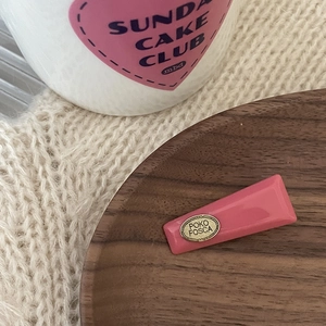 Pink macaron acrylic hair clip with gold metal plate on a cozy wooden setting