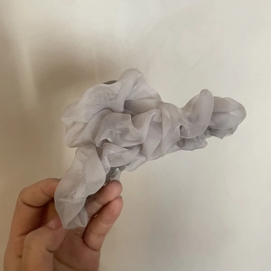 Detailansicht der eleganten grauen Haarspange aus Netzstoff mit Falten-Design in der Hand