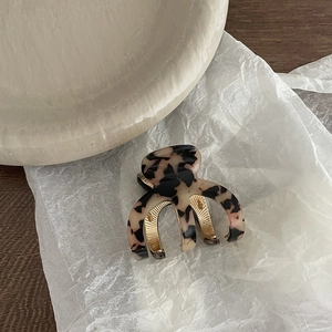 Détail d'une pince à cheveux en acétate léopard avec ressort doré sur papier blanc