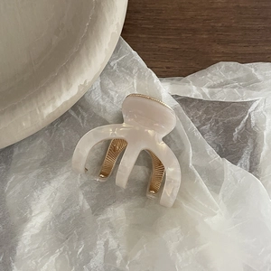 Pince à cheveux élégante en acétate crème avec dents en métal doré sur papier blanc