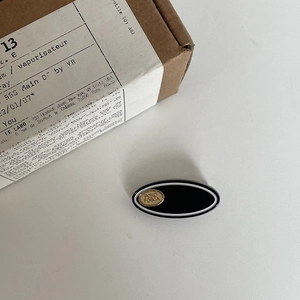 Minimalistische schwarze Acetat-Haarklammer mit goldenem Logo auf neutralem Hintergrund