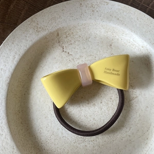 Détail d'un chouchou noeud jaune fait main avec boucle rose sur une assiette en céramique
