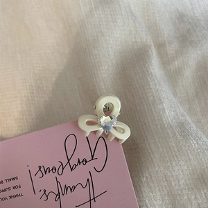 Close-up of mini cream-white hair claw clip with heart-shaped rhinestone on a pink card