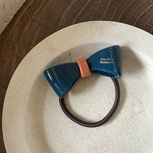 Détail d'un élastique à cheveux fait main avec nœud en acétate bleu et boucle orange