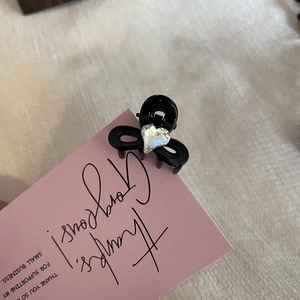 Close-up of a mini black heart rhinestone hair claw clip on a pink greeting card