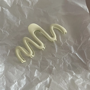 Macro shot of wave-shaped matte green hair claw clip on a white paper background