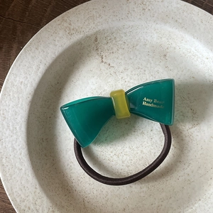 Détail d'un élastique à cheveux nœud vert fait main avec boucle jaune sur céramique