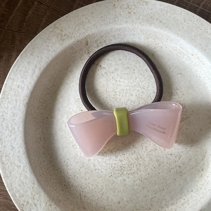 Détail de l'élastique à cheveux avec nœud en acétate rose et vert sur un plateau