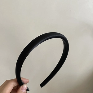 Gros plan d'un serre-tête en satin noir minimaliste tenu par la main sur un fond neutre