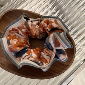 Gros plan d'un chouchou en satin fleuri avec motifs orange et gris sur plateau bois