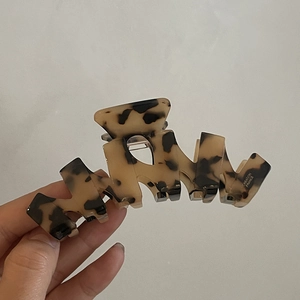 Dettaglio della molletta a tartaruga con scritta Creation France su sfondo beige