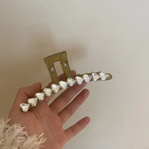 Brown translucent hair claw clip with crystal heart accents held by a hand
