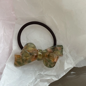 Macro shot of amber acetate bow hair tie on crinkled paper highlighting tortoiseshell texture