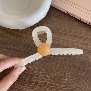 Detailed view of large cream acetate hair claw clip with a glossy orange amber-like bead