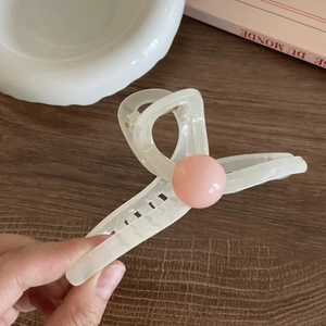 Detail of a large cream acrylic hair claw clip with a pink bead on a wooden surface