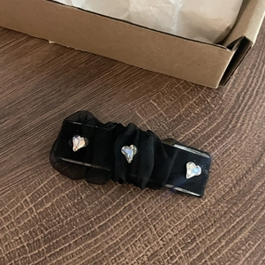 Detail of black mesh hair clip with pleated fabric and three heart-shaped crystals