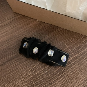Detail of black mesh hair clip featuring four sparkling clear crystals on wooden surface