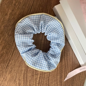 Detailed view of blue and white checkered scrunchie with cream scalloped piping edge