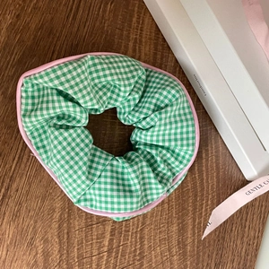 Detailed shot of green gingham scrunchie with pink trim on dark wood tabletop