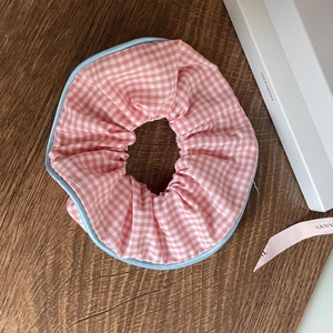 Flat lay of pink and white checkered scrunchie with light blue piping on a wooden surface