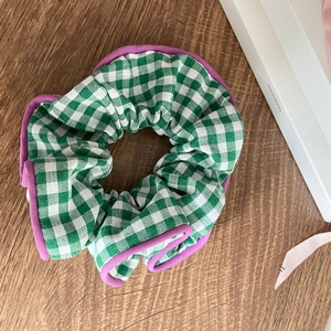Floral plaid scrunchie with green white check pattern and purple edge piping on wood