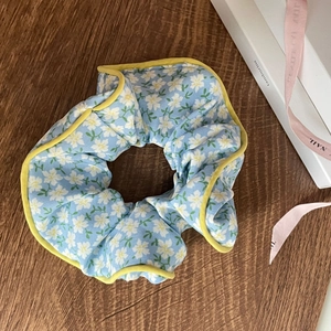 Detailed view of sky blue floral scrunchie with yellow piping on a rustic wooden background