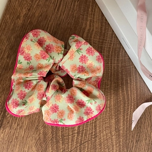 Detailed view of floral scrunchie with pink edges on a textured wooden background