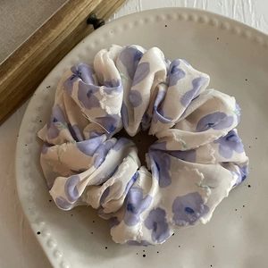 Chouchou élastique en mousseline fleurie violette sur un plateau en céramique blanche