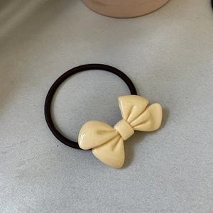 Detail view of a cream-colored bow hair tie with elegant marble texture and elastic band