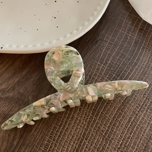 Grande pince à cheveux en acétate avec texture marbrée rose et verte sur table