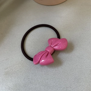 Close-up of pink glossy bow hair tie with high elastic black band on grey surface