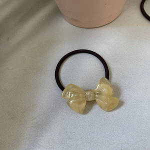 Top view of a cream yellow amber-textured resin bow hair tie with a dark brown elastic band