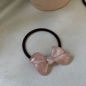 Close-up of a pink acetate bow hair tie with marble texture and black elastic band