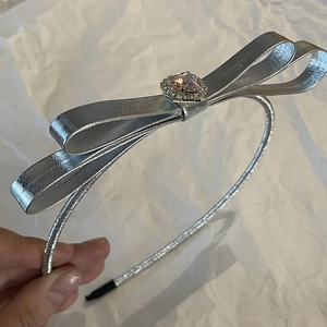 Silver metallic bow headband with a pink gemstone center and sparkling crystal accents