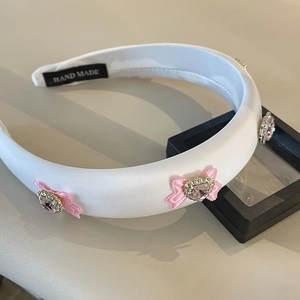 Elegant white padded headband featuring pink bows and heart crystals for hair styling