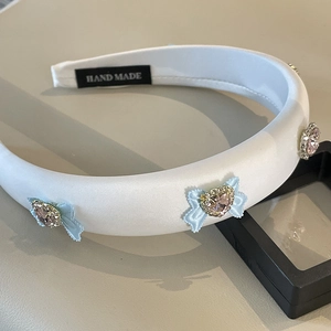 Detail of white satin headband featuring light blue bows and pink heart-shaped crystal centers