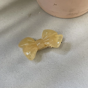 Détail d'une barrette à cheveux nœud en résine jaune crème avec pince crocodile dorée