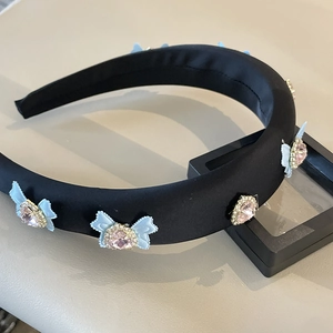 Close-up of black satin headband featuring light blue bow with a pink heart rhinestone