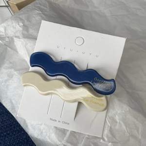 Close-up of wavy acetate hair clips in Klein blue and cream with gold lettering detail