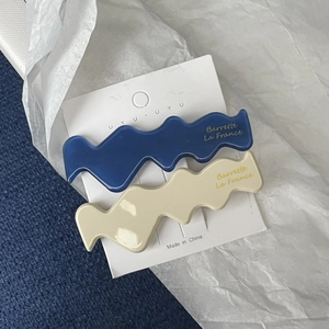 Blue and cream wave acetate hair clips with gold lettering on a display card