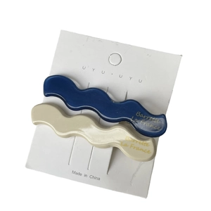 Klein blue and beige wave-shaped acetate hair clips with gold lettering on display card
