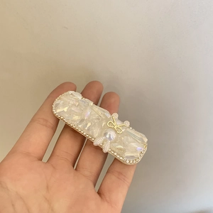 Barrette à cheveux en cristal avec nœud doré et perle tenue à la main