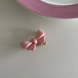 Detailopname van een roze strik haarclip van hars met een gouden metalen eendenbekklem