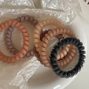 Matte spiralförmige Haargummis in verschiedenen Neutraltönen auf einem weißen Teller serviert