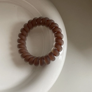 Matte kaffeebraune Spiral-Haargummis auf einem weißen Keramikteller präsentiert