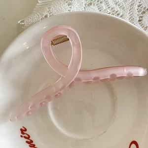 Détail d'une grande pince à cheveux rose mat dans un bol en céramique blanche et lumière douce