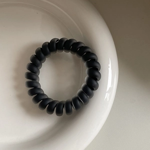 Matt schwarzes Spiral-Haargummi auf einem weißen Keramikteller in minimalistischer Optik