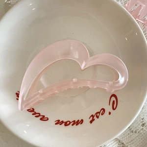 Pince à cheveux rose mat en forme de cœur présentée sur une assiette décorative blanche
