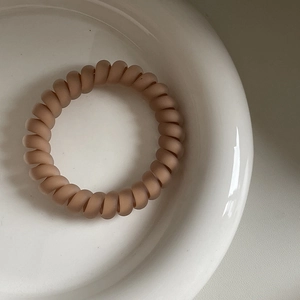 Nahaufnahme eines mattbeigen Spiralhaargummis in einer weißen Keramikschüssel